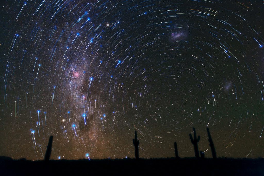 This gorgeous photograph, taken in the Atacama Desert in Chile, shows star trails circling the South Celestial Pole, over a cacti-dominated still landscape. The star trails show the apparent path of the stars in the sky as the Earth slowly rotates, and are captured by taking long-exposure shots. A final deeper exposure was superimposed over the magnificent trails, revealing many more, fainter stars and, just rising above the horizon, the southern Milky Way, with its patches of dark dust and the well-known pinkish glow of the Carina Nebula. Towards the right, the satellite galaxies of the Milky Way, the Large (top-centre) and Small (bottom-right) Magellanic Clouds, can also be seen.