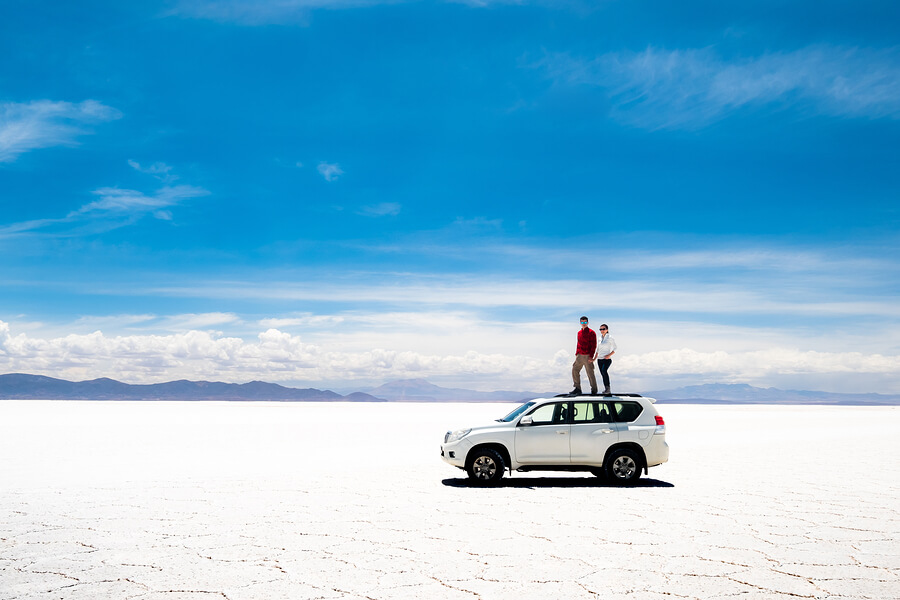 A picture of a couple standing on their car in the beautiful Salt Flats.